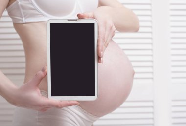 Hamile kadın tutarak ve dijital tablet ile boş göstermek Beyaz ahşap arka plan üzerinde gösterilen iç çamaşırı. Yakın çekim