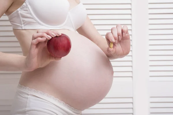 Mulher grávida em roupa interior segurando o comprimido em uma mão e uma maçã na outra. Alternativa à medicação . — Fotografia de Stock