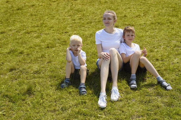 Mor och två unga söner sitter på gräset — Stockfoto