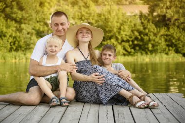 Mutlu genç aile, baba anne ve iki küçük oğlu nehir iskelede oturuyor