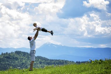 Mutlu baba küçük oğlu yeşil orman, dağlar ve gökyüzü bulutlu bir çerçevede yukarı atar. Babalık dostluk