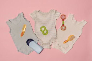 Pembe bir arka plan üzerinde üç bebek elbise ve bakım aksesuarları. Giysi kavramı