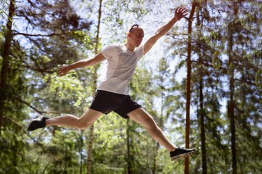 Genç adam bir iğne yapraklı orman içinde bir kaya üzerinde atlar. Aktif aşırı turizm