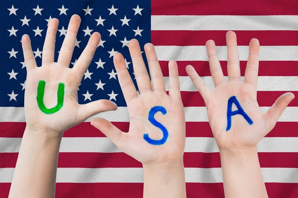 USA inscription on the children\'s hands against the background of a waving flag of the United States of America