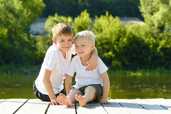 Dos niños pequeños se sientan en un abrazo a orillas del río. Concepto de amistad y fraternidad — Foto de Stock