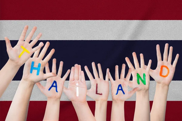 Thailändische Inschrift auf den Händen der Kinder vor dem Hintergrund einer wehenden thailändischen Fahne — Stockfoto