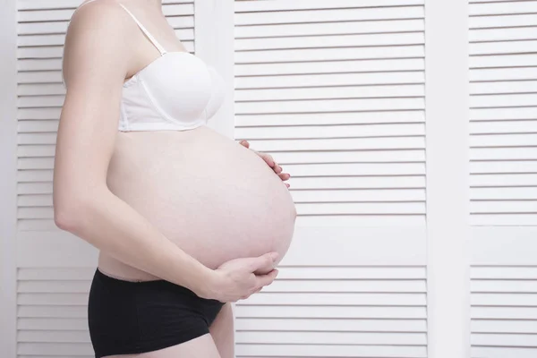 Kobieta w ciąży w bieliźnie tulenie brzuch z rąk na jasnym tle. — Zdjęcie stockowe