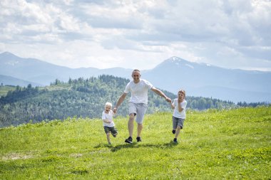 Baba ve yeşil orman, dağlar ve bulutlu gökyüzü arka plan üzerinde el ele tutuşarak yeşil alan çalışan iki genç oğlu.
