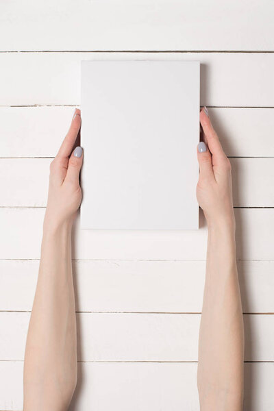 White rectangular box in female hands. Top view. White table on the background
