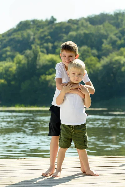 Dos niños pequeños se están abrazando en la orilla del río. Concepto de amistad y fraternidad — Foto de Stock