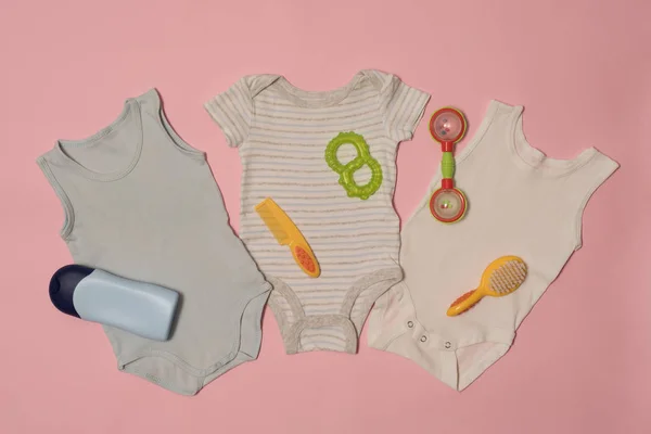Τρεις μωρό φορμάκι και φροντίδας αξεσουάρ σε ροζ φόντο. Έννοια ρούχα — Φωτογραφία Αρχείου