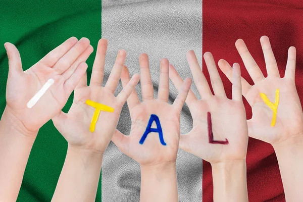 Italia iscrizione sulle mani dei bambini sullo sfondo di una bandiera sventolante dell'Italia — Foto Stock