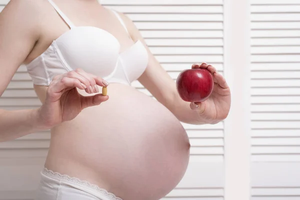 Hamile kadın bir yandan tablet ve diğer bir elma tutan iç çamaşırı. Alternatif ilaç. — Stok fotoğraf