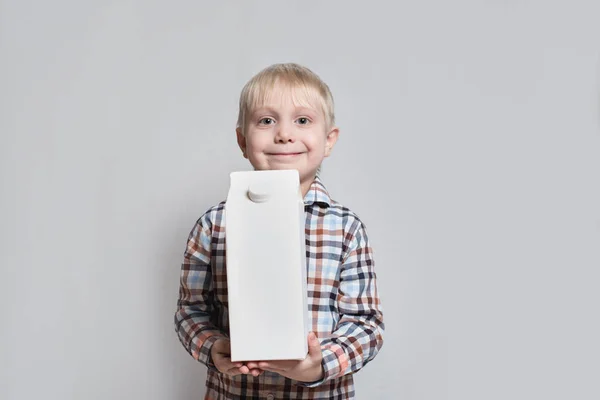 O menino louro feliz está segurando um grande pacote de caixa branca. Fundo de luz . — Fotografia de Stock