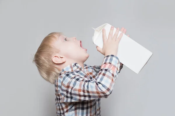 Il ragazzino biondo beve da un grosso pacchetto bianco. Sfondo chiaro — Foto Stock