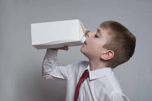 El niño bebe de un gran paquete blanco. Camisa blanca y corbata roja. Fondo claro —  Fotos de Stock