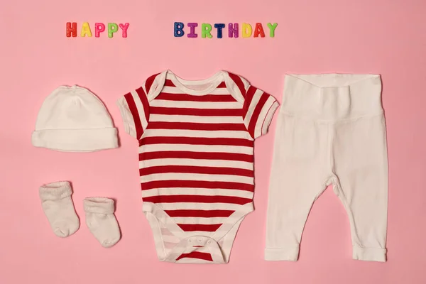 Conjunto de ropa para el recién nacido. Inscripción de colores feliz cumpleaños sobre un fondo rosa . —  Fotos de Stock