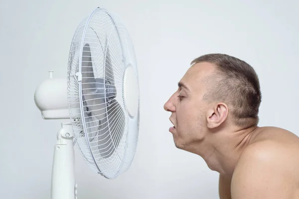 Man met stoppels op zijn gezicht lijdt aan de hitte en probeert af te koelen in de buurt van de ventilator. — Stockfoto