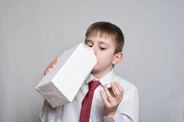 Ένα μικρό αγόρι πίνει από ένα μεγάλο λευκό πακέτο. Λευκό πουκάμισο και κόκκινη γραβάτα. Φως φόντο — Φωτογραφία Αρχείου