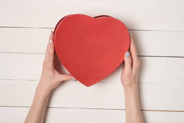 Kadın elleri Beyaz ahşap masa arka planına karşı kırmızı kalp şeklinde kutu tutun