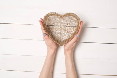 Kadın elleri beyaz ahşap bir masanın arka planına karşı metal tel şeffaf kalp şeklinde kutu tutun