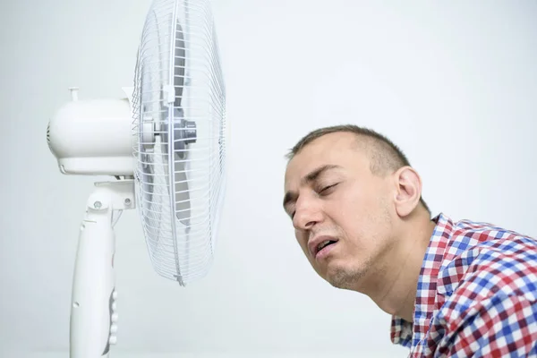 Hombre con rastrojo en su cara sufre del calor y tratando de refrescarse cerca del ventilador . —  Fotos de Stock