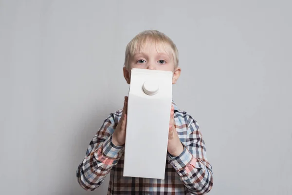 Il ragazzino biondo ha in mano un grosso pacco di cartone bianco. Sfondo chiaro . — Foto Stock