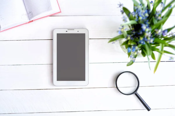 Tableta con pantalla vacía en negro. Cuaderno, lupa y flores en la mesa — Foto de Stock