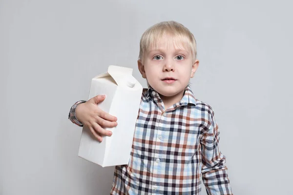 Kleine blonde jongen knuffels een groot wit karton pakket. Lichte achtergrond — Stockfoto