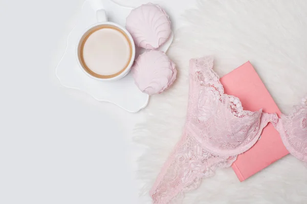 Cup of coffee with marshmallows. Pink lace bodice and notepad on white background. Fashionable concept. — Stock Photo, Image