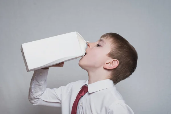 O rapazinho bebe de um grande pacote branco. Camisa branca e gravata vermelha. Fundo de luz — Fotografia de Stock