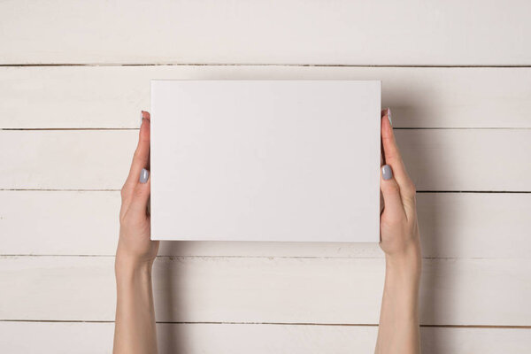 White rectangular box in female hands. Top view. White table on the background