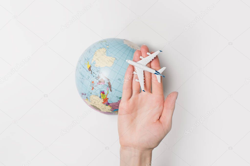 Passenger aircraft on the female palm on the background of the globe. Concept of air travel on a light background