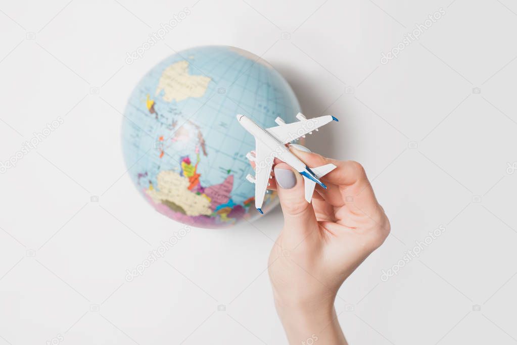 Passenger plane in a female hand on the background of the globe. Flight concept on a light background