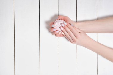 Beyaz ahşap arka planda nazik bir manikür ile kadın eller. Elinde Marshmallow