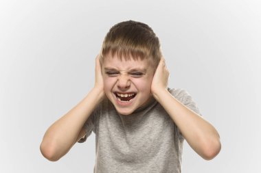 Çocuk elleriyle kulaklarını kapattı ve öfkeyle bağırıyor. Yaramaz bir okul çocuğu. Yalıt