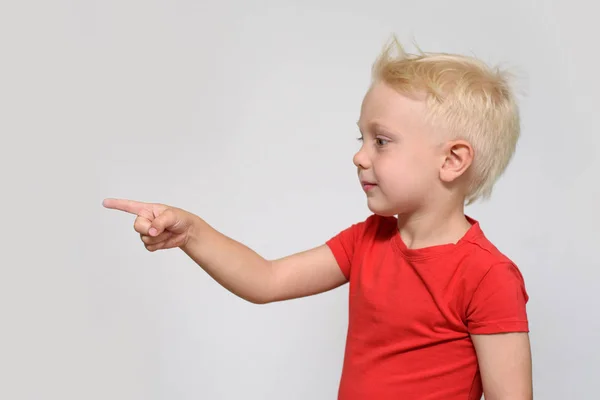 Little blonde boy in red t-shirt points his finger. Space for text. Place for advertising. White background — Stock Photo, Image