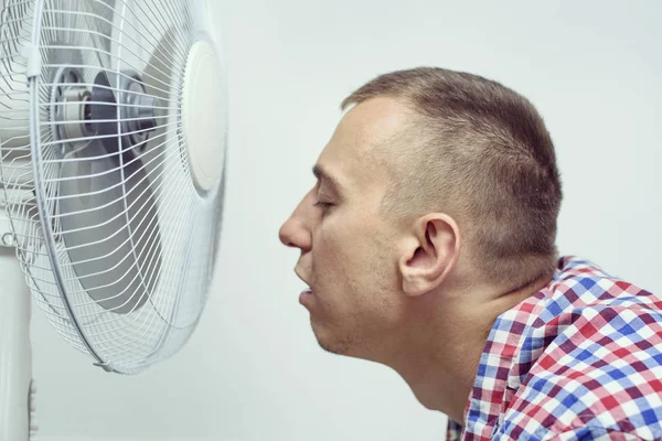 Man met stoppels op zijn gezicht lijdt aan de hitte en probeert af te koelen in de buurt van de ventilator. — Stockfoto