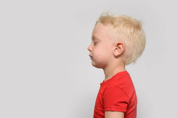 Kleine blonde jongen in rood t-shirt met gesloten ogen. Ruimte voor tekst. Witte achtergrond — Stockfoto