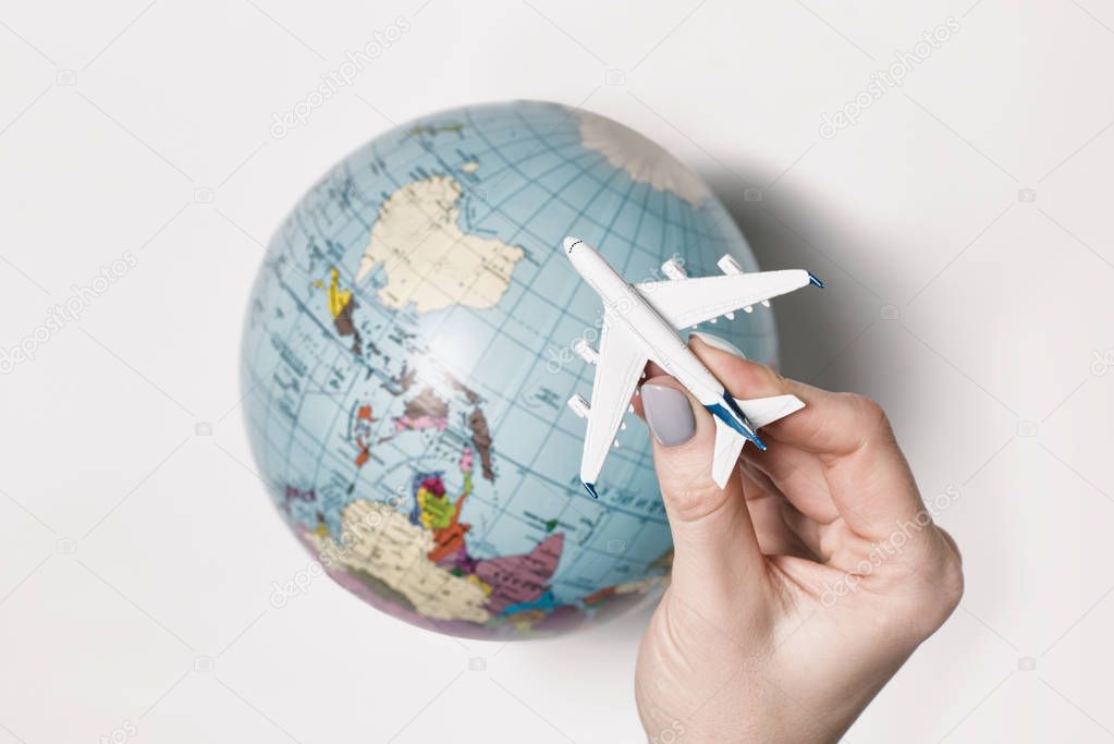 Passenger plane in a female hand on the background of the globe. Flight concept on a light background