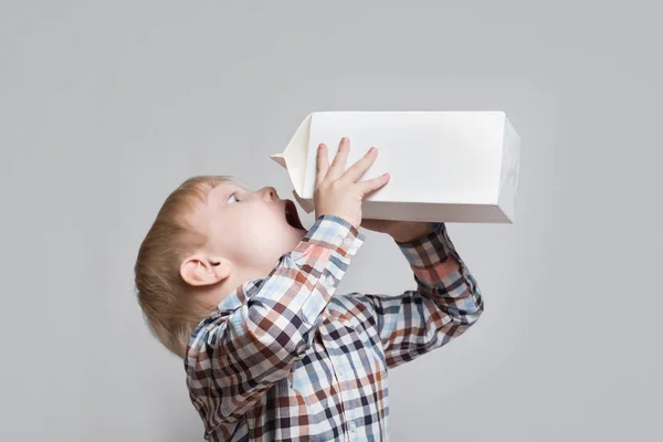 Το μικρό ξανθό αγόρι πίνει από ένα μεγάλο λευκό πακέτο. Φως φόντο — Φωτογραφία Αρχείου