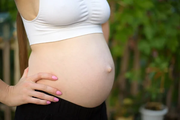 Hermoso vientre de una mujer embarazada, el sexto mes. Primer plano. Fondo de jardín — Foto de Stock