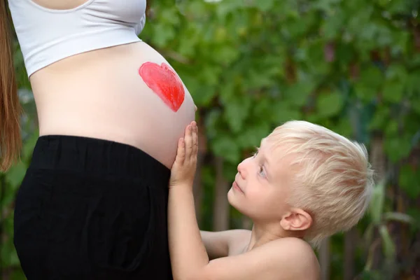 O menino loiro acaricia a barriga da mãe grávida. Conceito familiar — Fotografia de Stock