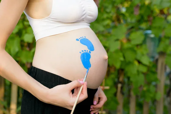 La mujer embarazada se dibuja en el vientre con la huella del bebé cepillo. Concepto de embarazada. Primer plano — Foto de Stock