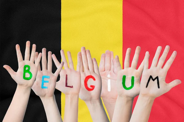 Inscription Belgium on the children's hands against the background of a waving flag of the Belgium — Stock Photo, Image