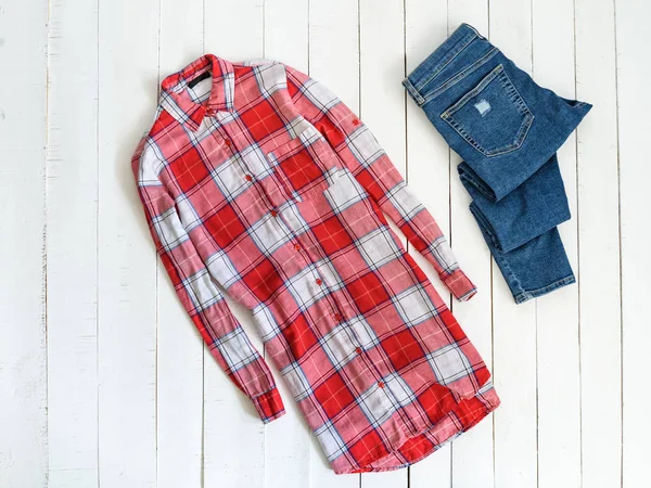 Conceito de roupa. Camisa quadriculada vermelha e branca e jeans em um fundo de madeira. Vista superior — Fotografia de Stock