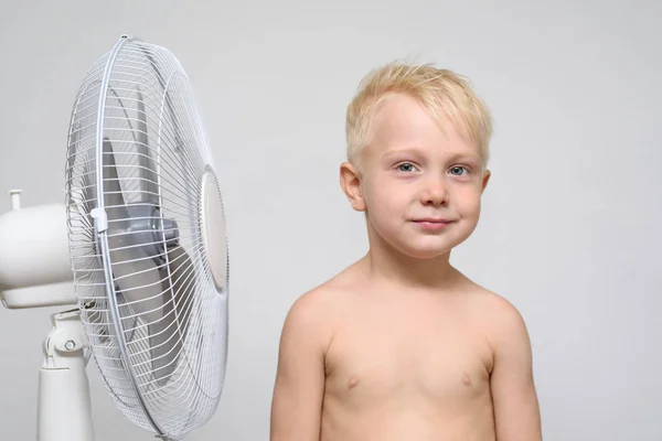 Rapaz louro muito sorridente com tronco nu fica perto de um ventilador. Conceito de verão — Fotografia de Stock