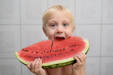 Küçük sarışın çocuk büyük bir karpuz parçası yiyor. Yaz konsepti. Ev iç