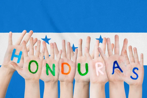 Inscrição Honduras nas mãos das crianças contra o pano de fundo de uma bandeira acenando das Honduras — Fotografia de Stock