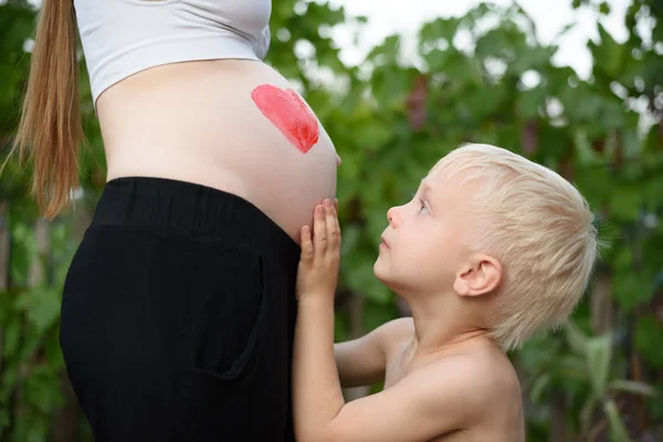 Mały blond chłopiec uderzeń brzuch jego matki w ciąży. Koncepcja rodzinna — Zdjęcie stockowe